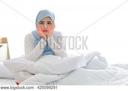 Beautiful And Young Asian Muslim Woman In Sleepwear With Tooth Pain Emotion Sitting On Bed. Cute Gir