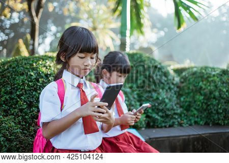 Asian Primary Student Using Mobile Phone In School Park