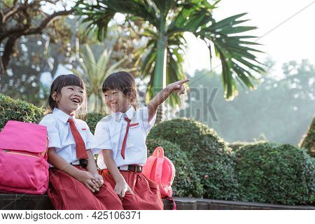 Two Asian Student In Uniform Pointing Away While Sitting Togehter