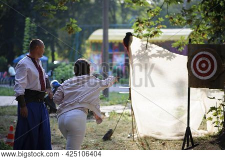 Girl Throws Knives At A Wooded Target. Woman With Red Hair Throwing Knife At Bullseye Target With A 