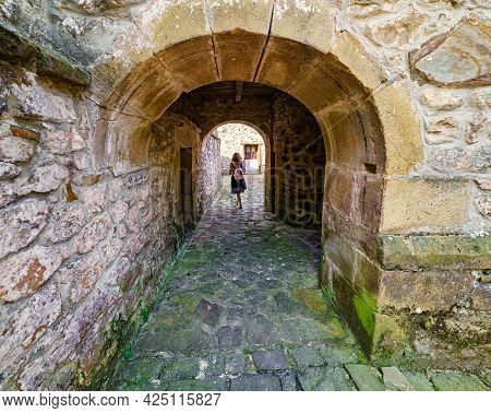 Woman Crossing An Arched Tunnel Under An Old Stone Building. Barcena Mayor Santander.