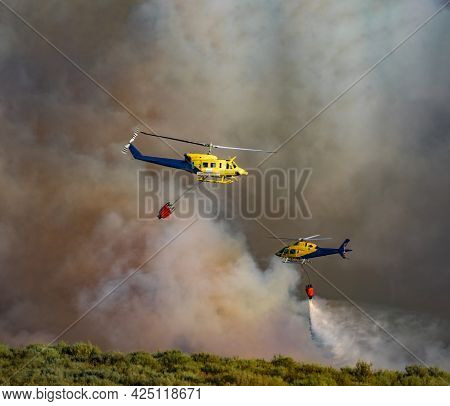 Two Helicopters With Bambi Bucket Working On Fire Extinction