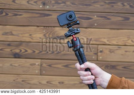 Compact Action Camera On A Flexible Tripod In Hand On A Wooden Background.
