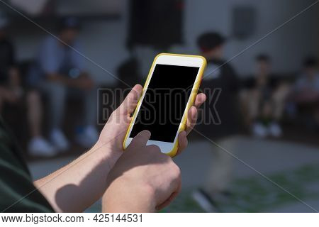 The Guy Holds A Mock-up Of A Smartphone In His Hand Against The Background Of The Children's Dance C