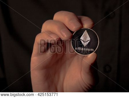 Ethereum Silver Crypto Coin In Male Hand Over Black Background. Eth Or Etherum.