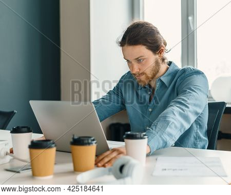 Pensive Young Man In Casual Outfit Looking At Laptop Screen During Work In Office, Thoughtful Seriou