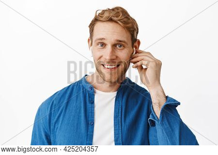 Close Up Of Handsome Redhead Man Wears Wireless Earphone And Smiles At Camera, Talks With Someone In