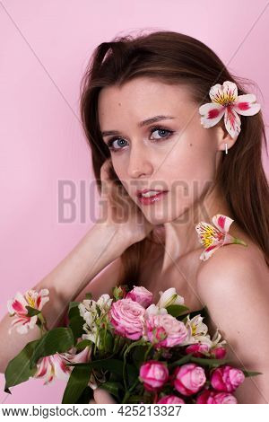 Naked Skinny Girl Holding Flowers On A Pink Background. Brunette