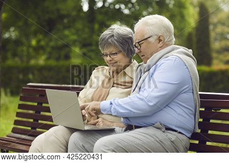 Happy Senior Couple Using A Laptop Computer While Sitting On A Park Bench Together