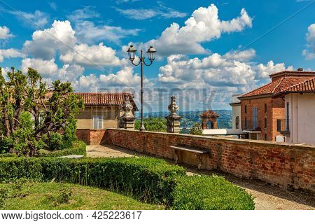 Green bushes in the park and typical houses under beautiful blue sky with white clouds in small town of Govone in Piedmont, Northern Italy.