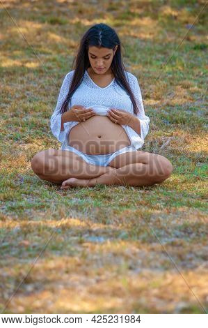 Young Pregnant Woman Sitting On The Grass Looking At Her Tummy