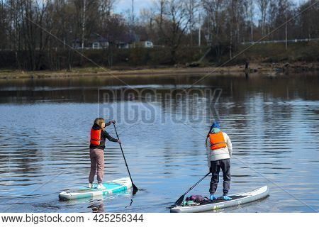 Vyborg, Russia, May 2, 2021-young Women In Sports Outfit And Orange Life Vests Surf On Supboards In 