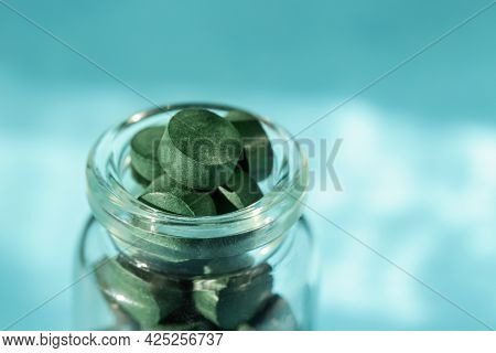 Spirulina Pills In Glass Bottle On Blue Background. Antioxidant Nutrition. Copy Space