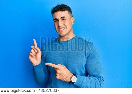 Hispanic young man wearing casual winter sweater pointing aside worried and nervous with both hands, concerned and surprised expression 