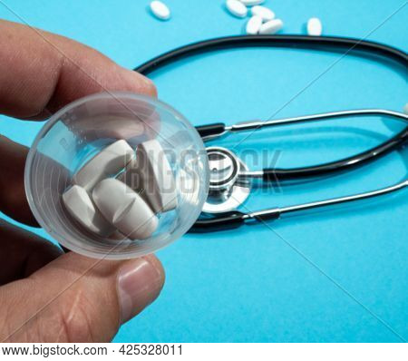 Close Up Of A Man Holding A Pill On A Blue Background. The Stethoscope Lies On A Blue Background.
