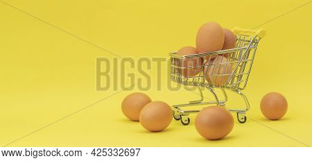 Raw Chicken Eggs In A Basket On A Yellow Background. Eggs In A Metal Cart On A Yellow Background. Ba