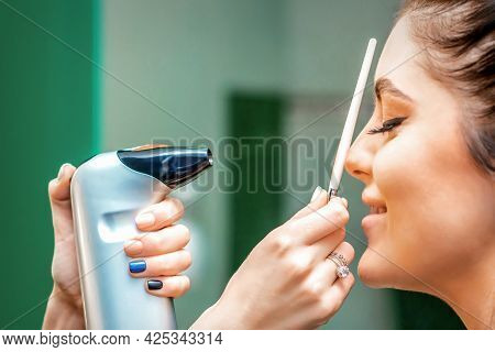Side View Of A Make-up Artist Using Aerograph Making An Airbrush Makeup Foundation On A Female Face 