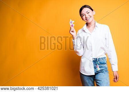 Beautiful Asian Girl In A Shirt And Jeans Smiling Holding A Siple Dimple Toy In Her Hand