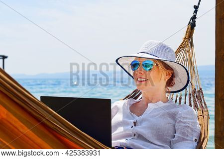 Work From Anywhere. Young Smilyng Woman, Female Freelancer In Straw Hat Working On Laptop On Beach.