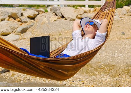 Work From Anywhere. Young Smilyng Woman, Female Freelancer In Straw Hat Working On Laptop On Beach.