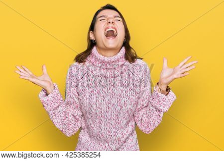 Young caucasian girl wearing wool winter sweater crazy and mad shouting and yelling with aggressive expression and arms raised. frustration concept. 