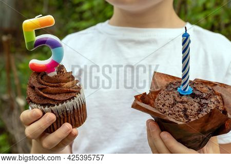 A Boy In A White T-shirt Holds Sweets With Candles On The Background Of The Garden. Celebration Of T