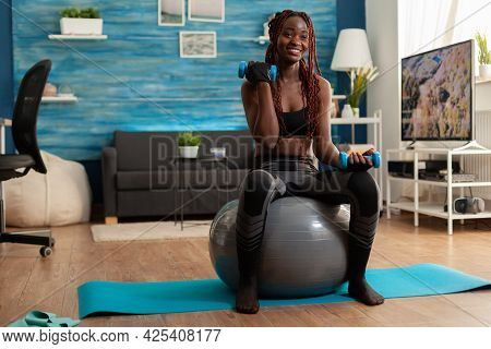Joyful Athletic Black Person In Leggings Using Stability Ball For Training Biceps, Doing Curls With 