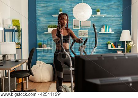 African Fit Strong Woman Doing Cardio Exercise On Eliptical Machine, In Home Living Room Looking At 