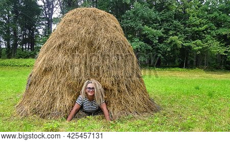 Pretty Woman With Curly Hair Peeking Out Of A Haystack Standing In The Meadow In Aluksne, Latvia