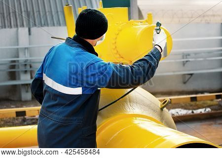 A Painter In Working Clothes Paints A Metal Shut-off Valve For Gasification From A Compressor Gun On