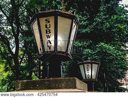 Side angle shot of an old fashioned lamp on a short pole near another lamp with the inscription \