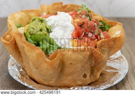 Huge Tostada Crispy Bowl Filled Completely And Topped With Scoops Of Sour Cream, Guacamole, And Pico