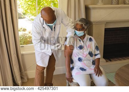 Senior african american woman and male doctor in face masks, woman receiving vaccination. retirement and senior lifestyle during covid 19 pandemic concept.