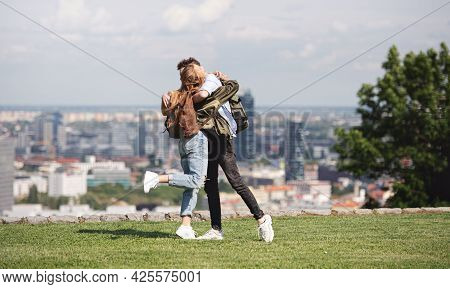 Young Couple Travelers In City On Holiday, Hugging. Cityscape In The Background.
