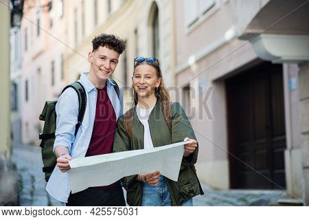 Young Couple Tourists Travelers With Map In City On Holiday, Looking At Camera.