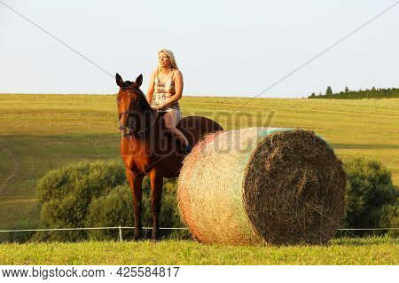 Lady With Horse Near Hayroll On Meadow In Summer Day