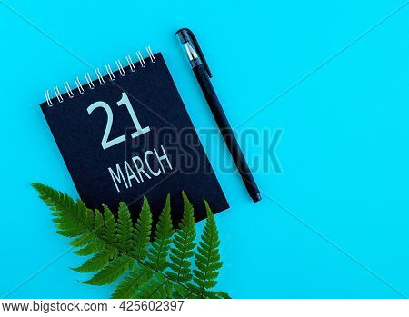 March 21th. Day 21 Of Month, Calendar Date. Black Notepad Sheet, Pen, Fern Twig, On A Blue Backgroun