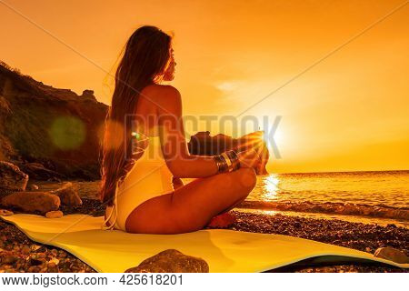 Young Woman With Long Hair In White Swimsuit And Boho Style Braclets Practicing Outdoors On Yoga Mat