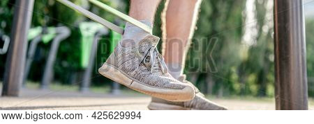 Closeup view of legs feets of man guy training with elastic rubber band at the stadium outdoors. Adult male person during workout with additional sport equipmant