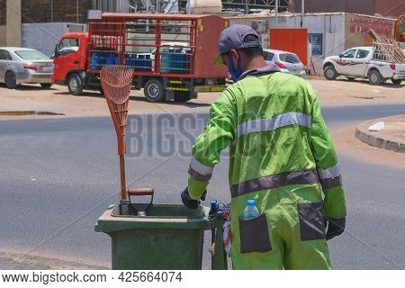Street Cleaner, Back View To Arab Origin Man In Uniform Collecting Street Rubbish To Dumpster During