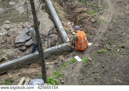 Man In Orange Vest While Installing Street Curbstone