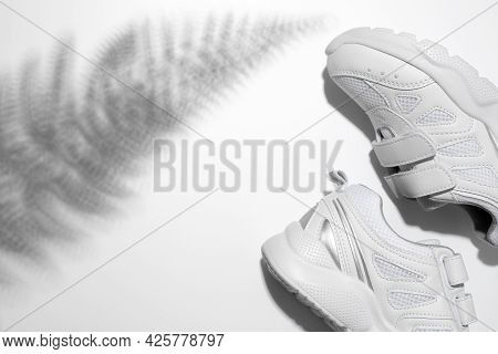Top View Partially Two White Sneakers On The Side With Hard Summer Sunny Fern Shadows On A White Bac