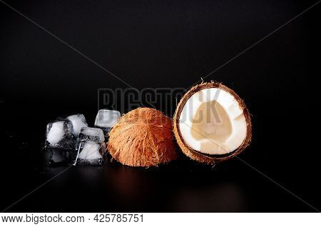 Broken Coconut With Melted Ice Cubes On A Black Background.