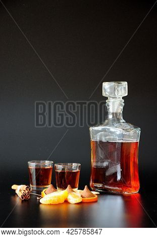 A Glass Decanter And Two Glasses Of Brandy, Chocolates, Cinnamon And Tangerine Slices And Zest On A