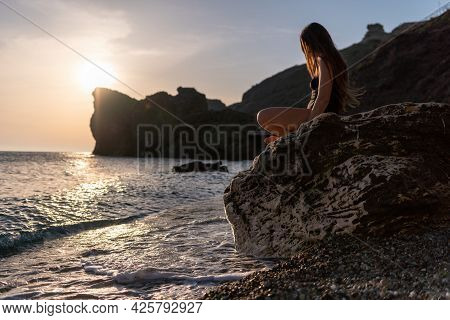 Young Woman With Long Hair In Black Swimsuit And Boho Style Braclets Practicing Outdoors On Yoga Mat