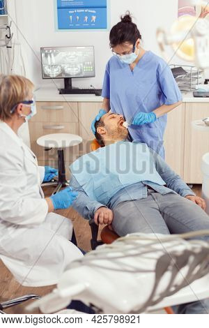 Stomatologist Nurse Looking In Patient Mouth Preparing For Dental Surgery. Dentist Asisstant With Fa