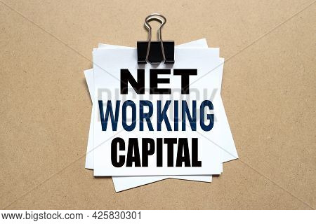 Net Working Capital. The Paper Is Clamped With A Clerical Clip. Paper On Wood Background.