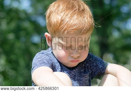 The Child Is Offended. Portrait Of A 4-year-old Red-haired Boy Who Sits In The Sun And Takes Offense