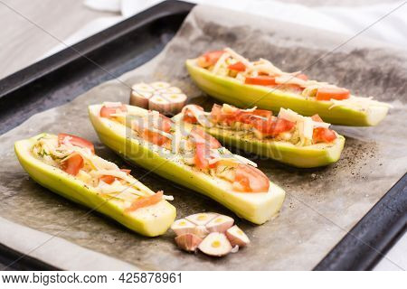 Raw Zucchini Halves, Ready To Bake, Stuffed With Cheese And Tomato On Baking Paper On A Baking Sheet