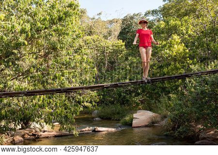 Lady In Red Standing On Small Make Shift Bridge Over The Rio Das Almas In The Interior Of Brazil